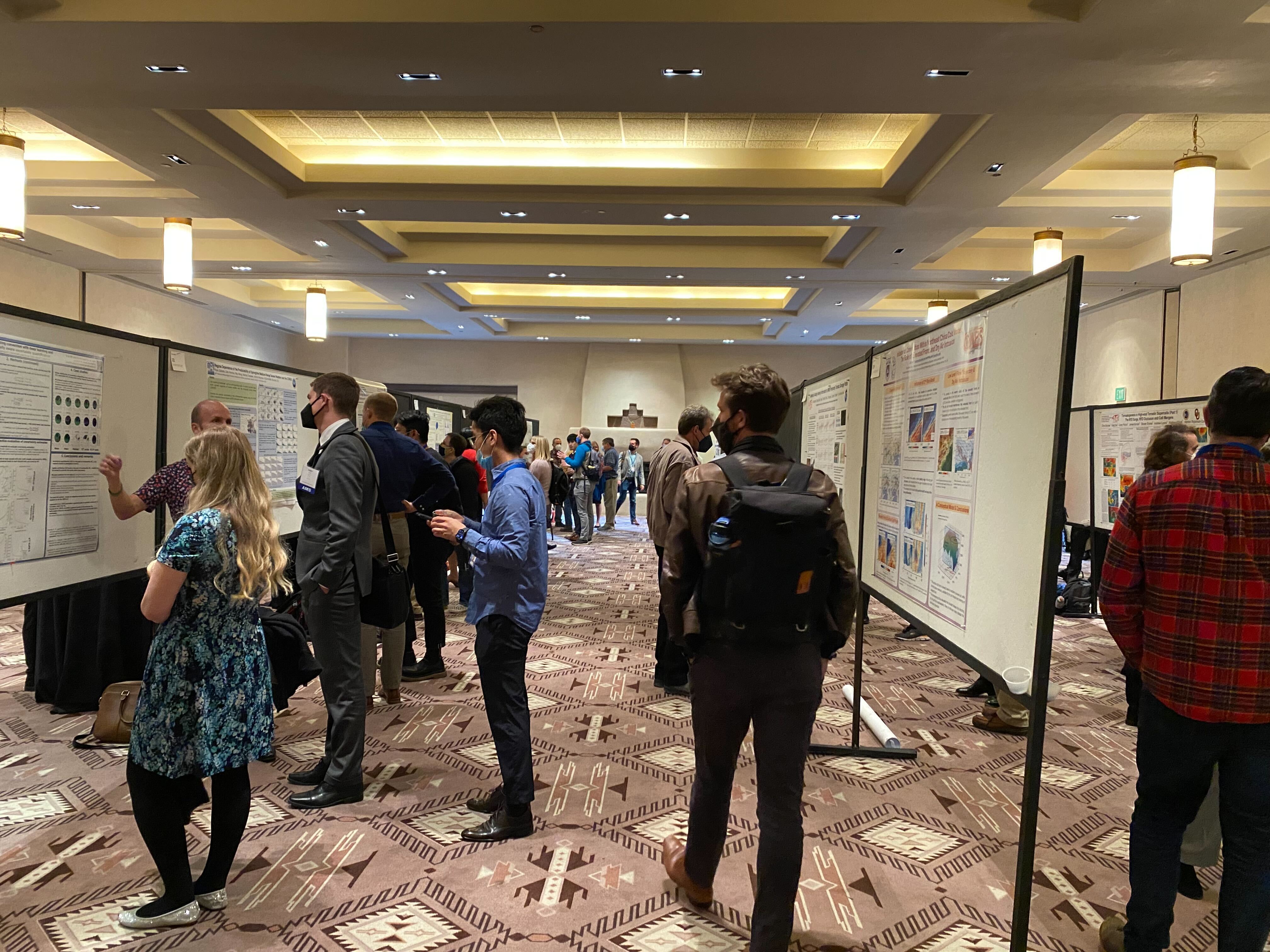 A conference room with several attendees examining and discussing scientific posters displayed on boards. The atmosphere is engaged and collaborative.